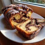 A freshly baked chocolate babka loaf, sliced to show the rich swirl of filling, drizzled with white icing.