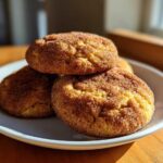 A stack of three perfectly baked snickerdoodle cookies, coated in cinnamon sugar, sitting on a light blue plate.