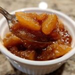A spoonful of rich, spiced apple pie filling being lifted from a small white ramekin.
