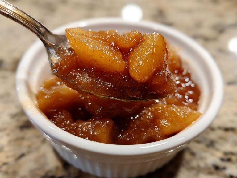 A spoonful of rich, spiced apple pie filling being lifted from a small white ramekin.