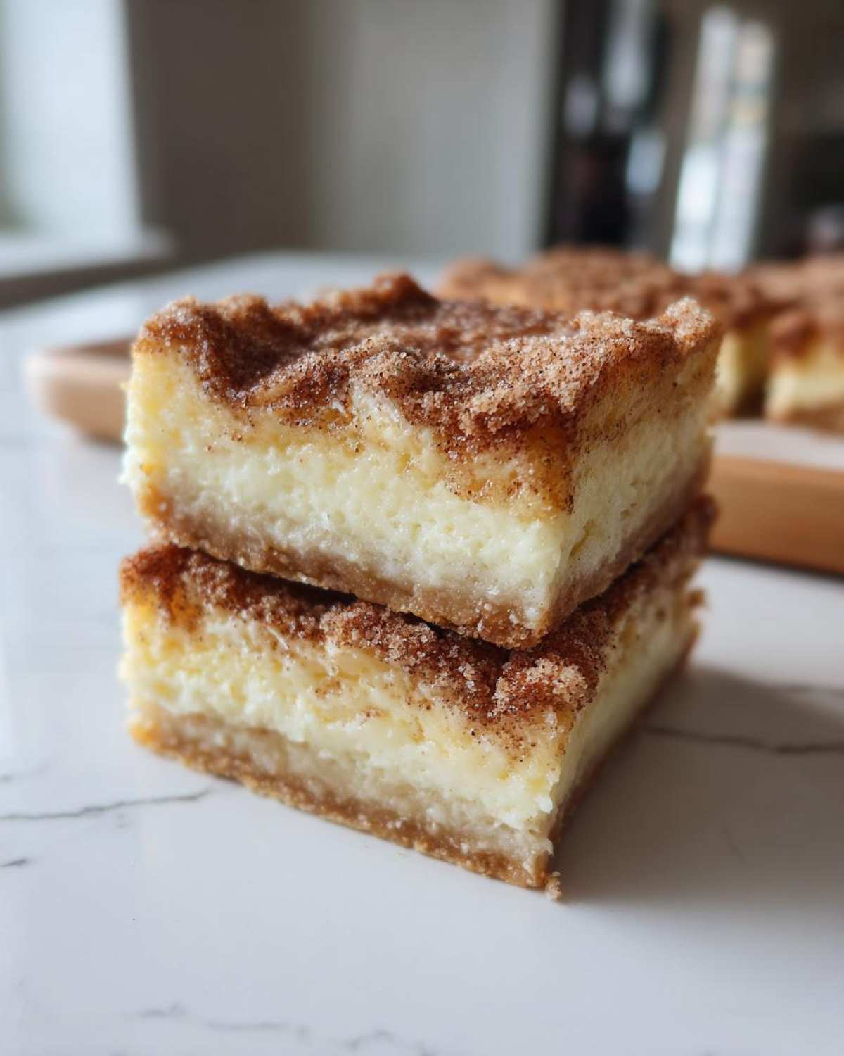 Two stacked squares of creamy churro cheesecake bars topped generously with cinnamon sugar.