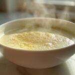 Close-up of a steaming white bowl filled with creamy cauliflower soup, garnished with spices.
