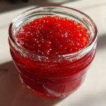Close-up of a glass jar filled with vibrant red strawberry freezer jam, showing visible seeds.