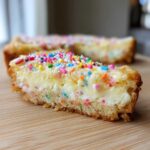 Close-up of a slice of sugar cookie cheesecake bars topped with colorful sprinkles.