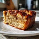 Close-up of a square slice of moist swedish apple cake with a caramelized, glossy apple topping.