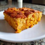 A close-up, appetizing slice of moist sweet potato cobbler with a golden-brown top, served on a white plate.