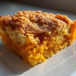 Close-up of a square slice of vibrant orange sweet potato cobbler with a crumbly, golden-brown topping.