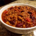 Close-up of a white bowl filled with rich, thick high protein chili featuring ground meat and kidney beans.