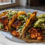 Three grilled salmon tacos filled with slaw and topped generously with chunky guacamole.