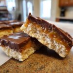 Close-up of two twix cookies bars cut in half, showing the shortbread base, gooey caramel, and chocolate topping.