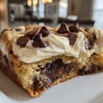 Close-up of a thick slice of cookie cake recipe topped with creamy frosting and chocolate chips.