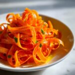 Close-up of vibrant orange ribboned carrots in a white bowl, making up a delicious raw carrot salad.