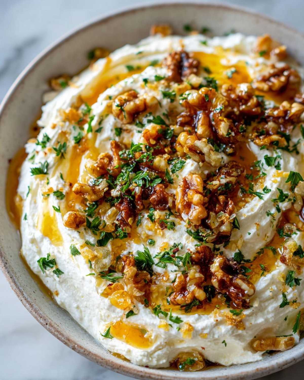 A close-up of creamy whipped ricotta dip topped with toasted walnuts, a drizzle of honey, and fresh parsley.