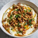 A bowl of creamy whipped ricotta dip generously topped with candied walnuts, olive oil, and fresh parsley.