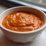 A close-up view of thick, vibrant orange chili cheese dip served in a small white ramekin.