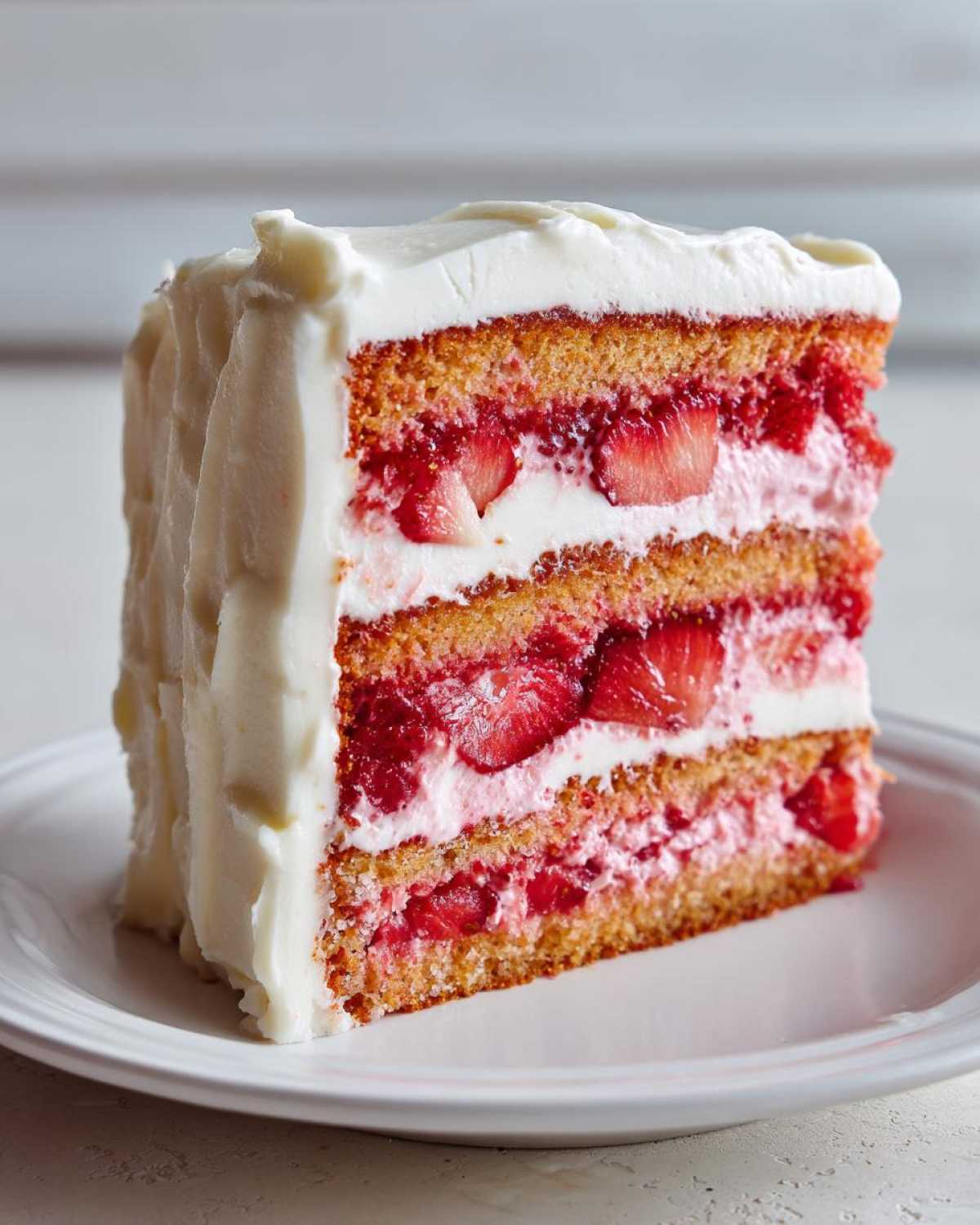 A tall, moist slice of 3-layer strawberry cake filled with fresh strawberries and white frosting.