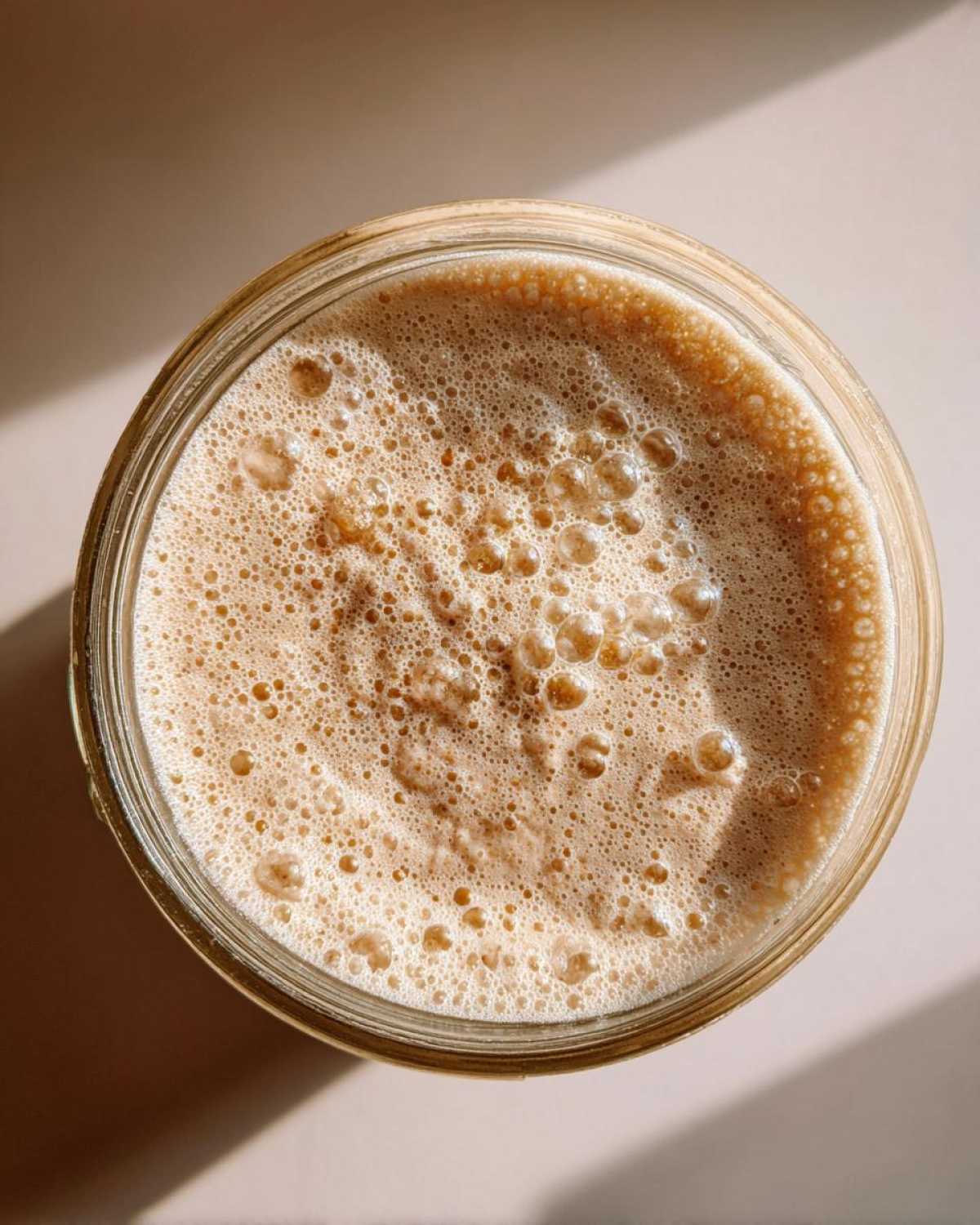 Overhead view of an active sourdough starter in a glass jar, showing a thick layer of small, active bubbles.