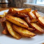 A close-up of a white plate piled high with golden, crispy seasoned air fryer potato wedges.