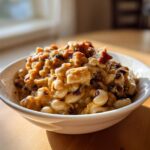 A close-up of a white bowl filled with creamy, savory black eyed peas and chunks of meat, bathed in sunlight.
