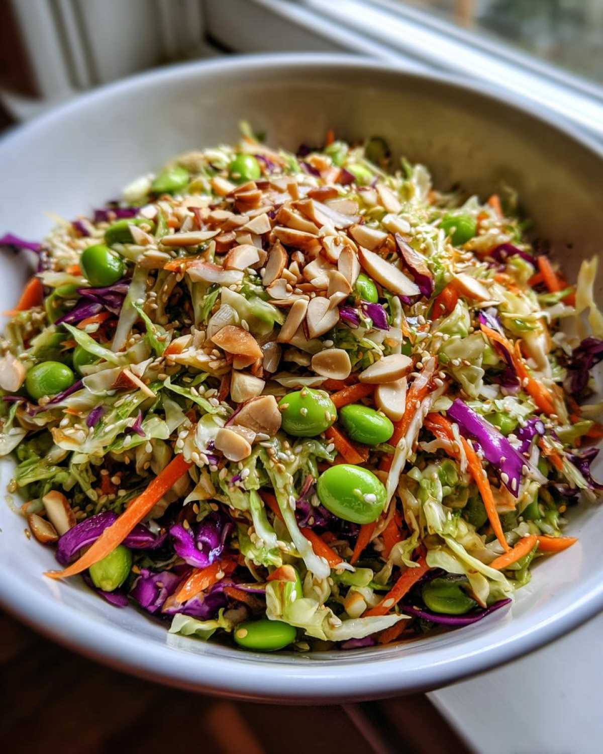 Close-up of a vibrant cabbage salad featuring shredded green and purple cabbage, carrots, edamame, and topped with slivered almonds.