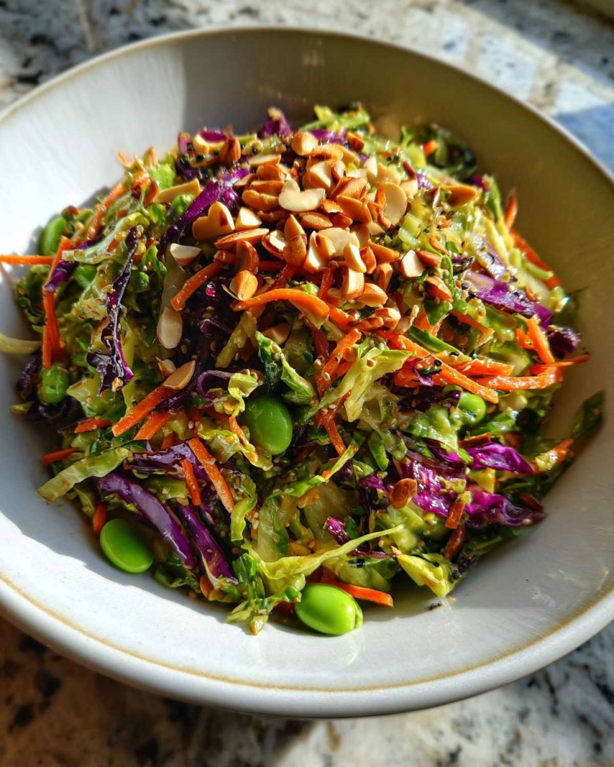 Close-up of a colorful cabbage salad topped with slivered almonds and edamame.