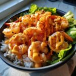 Close-up of a delicious shrimp bowl featuring seasoned shrimp drizzled with creamy sauce over white rice and lettuce.