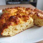 Close-up of a thick, fluffy keto pizza crust slice showing its airy interior and golden-brown, cheesy top.