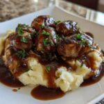 A close-up of delicious bangers and mash, featuring sausages covered in brown onion gravy over creamy mashed potatoes.
