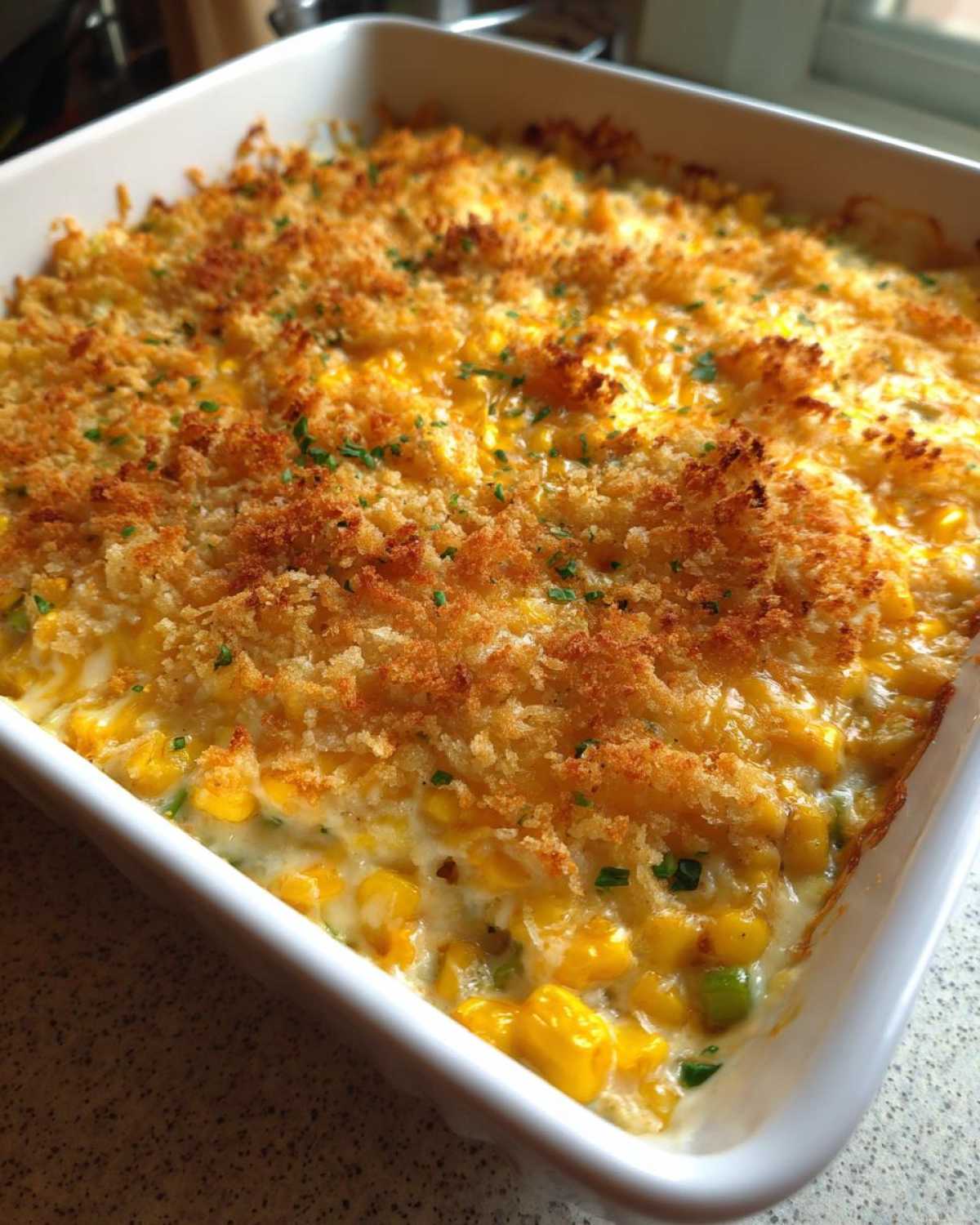 A close-up of a creamy, cheesy corn dip baked in a white casserole dish with a golden brown, crispy breadcrumb topping.