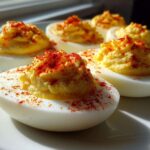 Close-up of several perfect deviled eggs on a white plate, topped with creamy filling and sprinkled with bright red paprika.