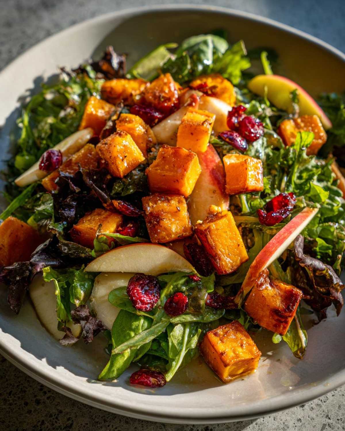 Close-up of a vibrant fall harvest salad featuring roasted butternut squash cubes, apple slices, and dried cranberries.