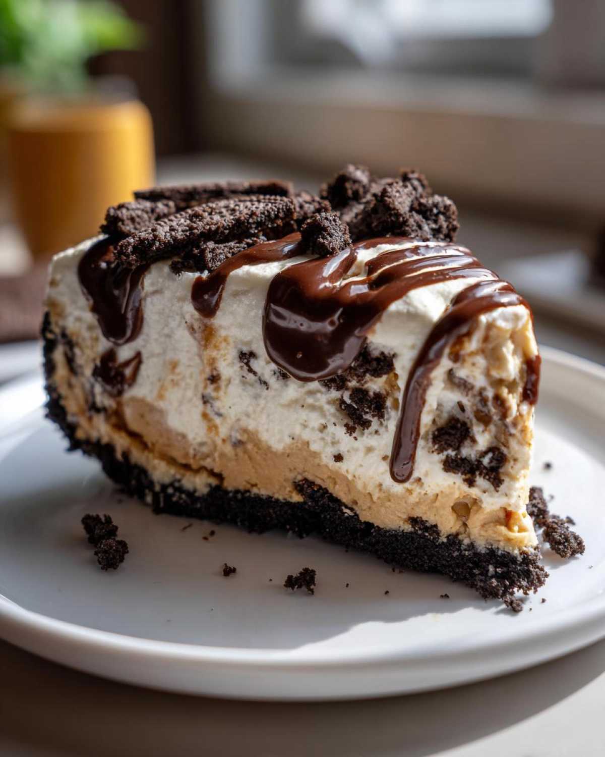 A decadent slice of ice cream pie featuring layers of peanut butter and cream, topped with chocolate fudge and cookie crumbles.