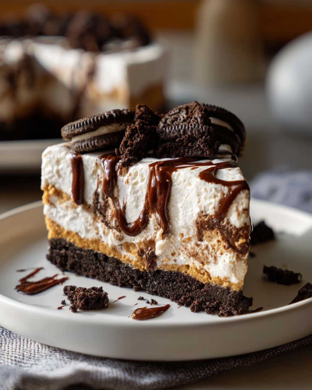 A decadent slice of ice cream pie featuring a dark crust, peanut butter layer, whipped topping, and chocolate drizzle, topped with Oreos.