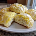 A plate of soft ricotta cookies topped with a thick, glossy lemon glaze, one cookie is broken open.