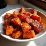 Close-up of caramelized, cubed roasted sweet potatoes sprinkled with seasoning in a white bowl.