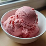 Two scoops of vibrant pink strawberry ice cream served in a white bowl.