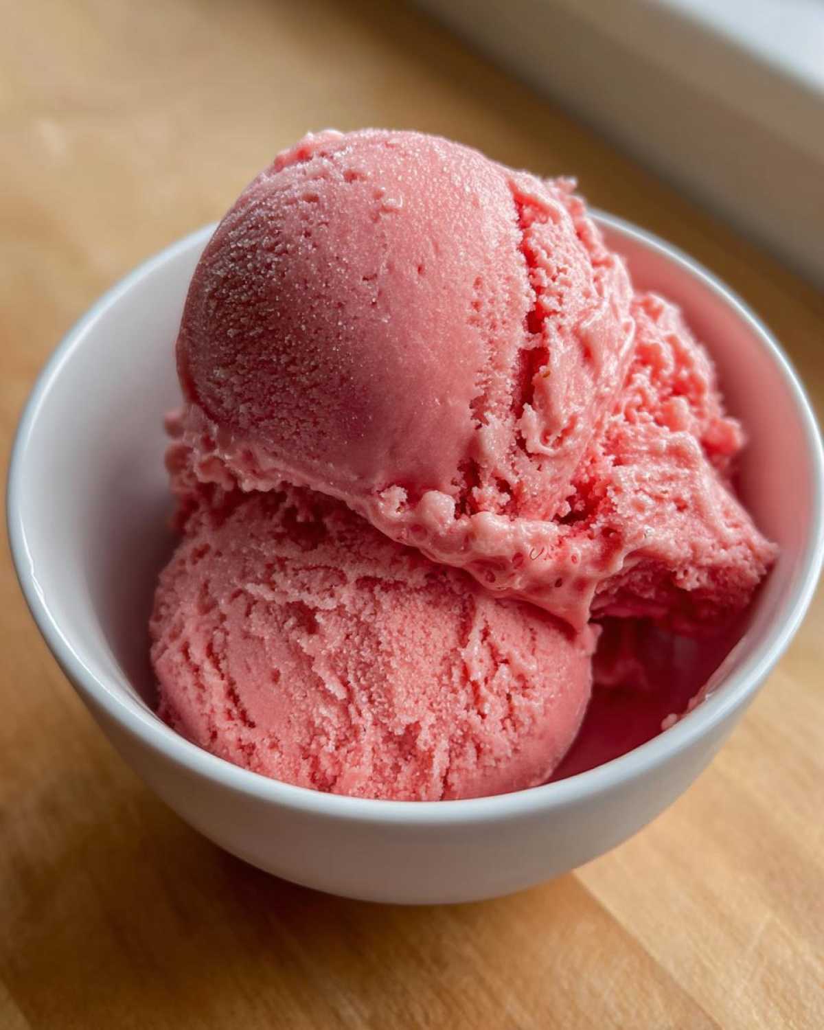 Two scoops of bright pink, slightly frosty strawberry ice cream served in a small white bowl.