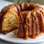 Close-up of a slice cut from a bundt-style apple dapple cake, heavily drizzled with thick caramel sauce.