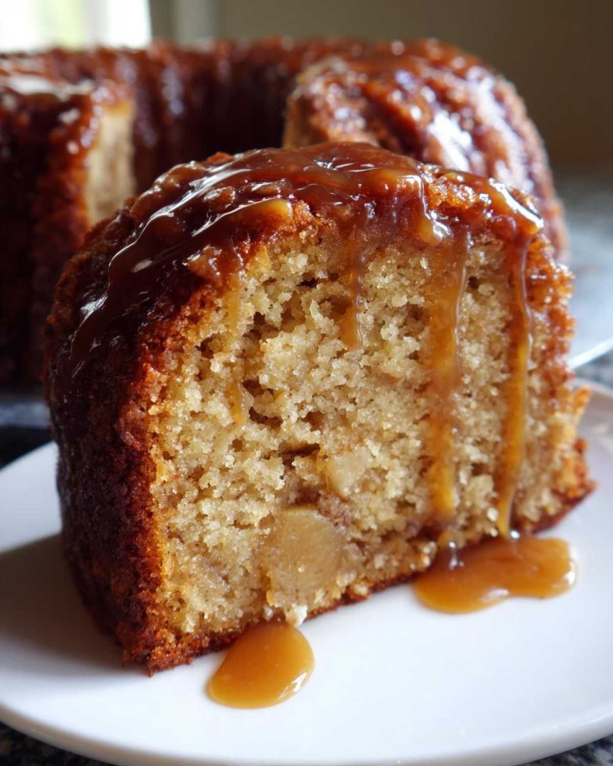 Close-up of a moist slice of apple dapple cake topped generously with dripping caramel sauce.