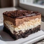 A rich, layered slice of Baileys Chocolate Cheesecake Trifle showing a dark crust, white filling, and chocolate mousse top.