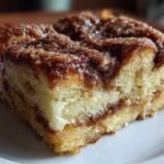 A moist, square slice of baked french toast with a rich cinnamon swirl topping, served on a white plate.