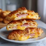 A stack of three halves of baked ham and cheese croissants showing melted cheese and ham layers.