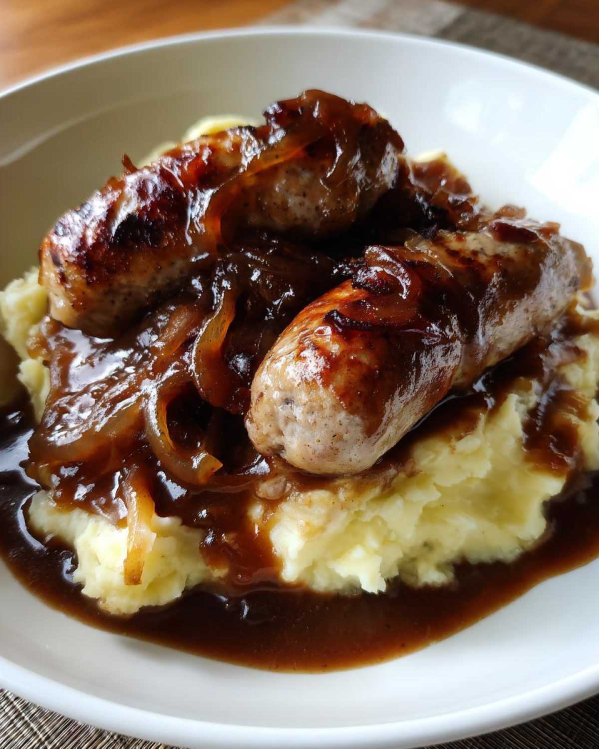 Close-up of two browned sausages served over creamy mashed potatoes, smothered in onion gravy for bangers and mash.