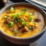 Close-up of a bowl of creamy Cajun potato soup topped with shredded cheddar cheese and fresh green onions.