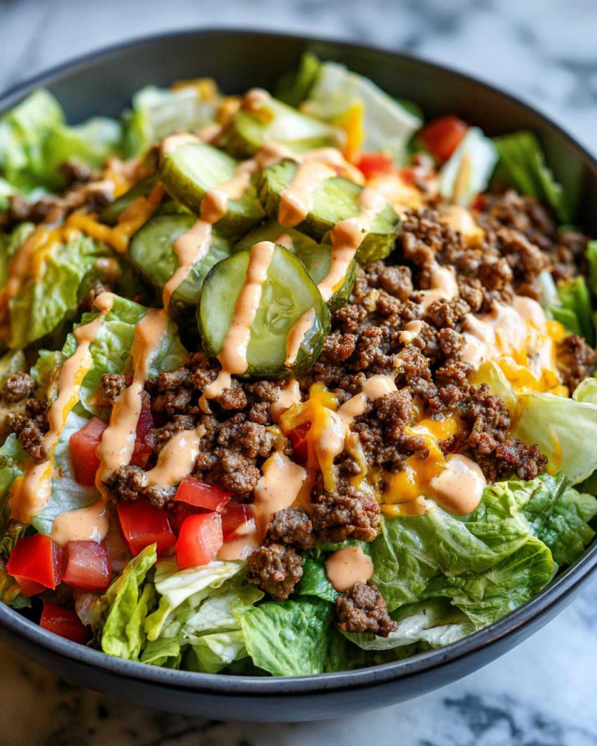 A close-up view of a vibrant cheeseburger bowl featuring lettuce, seasoned ground beef, pickles, and a drizzle of special sauce.