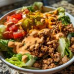 A vibrant cheeseburger bowl featuring seasoned ground beef, lettuce, tomatoes, cheese, and special sauce.