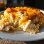 A close-up serving of cheesy chicken and rice casserole topped with melted cheddar cheese.