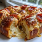 Close-up of cheesy pepperoni pizza sliders baked together, showing a dramatic cheese pull.