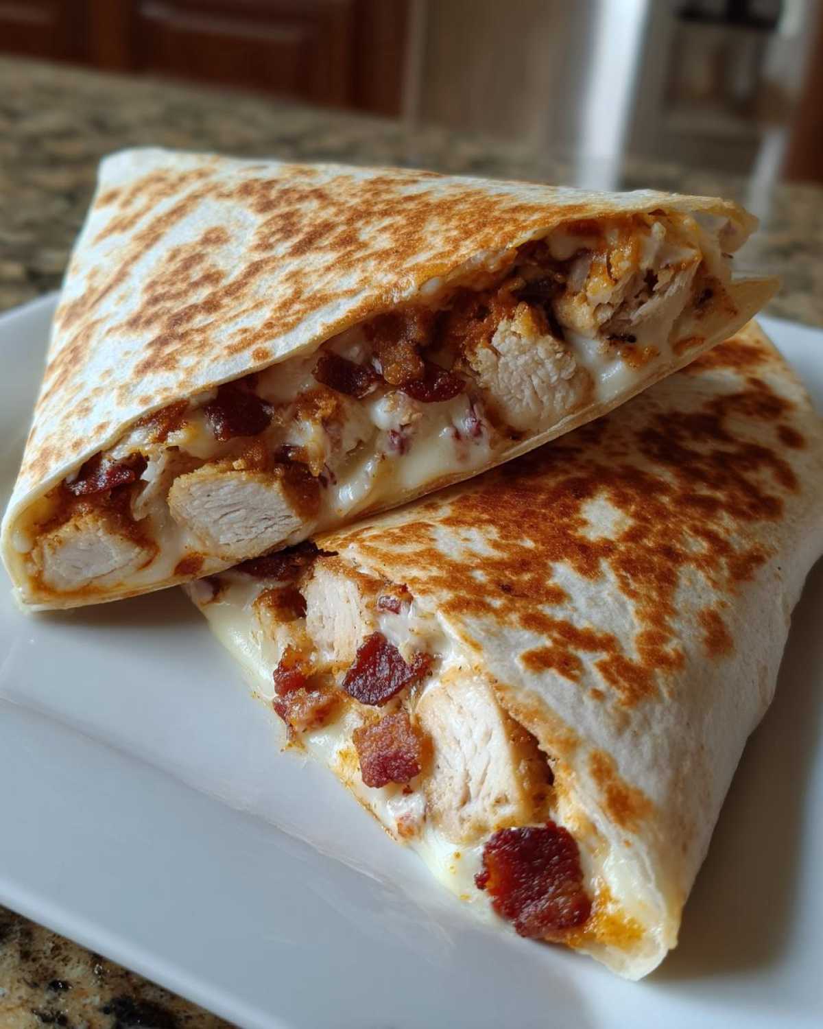 Close-up of a grilled chicken bacon ranch wrap cut in half, showing melted cheese, chicken chunks, and bacon bits.