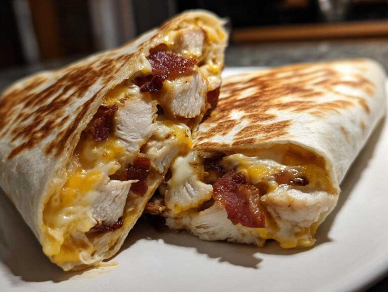 Close-up of a grilled chicken bacon ranch wrap cut in half, showing chunks of chicken, bacon, and melted cheese.